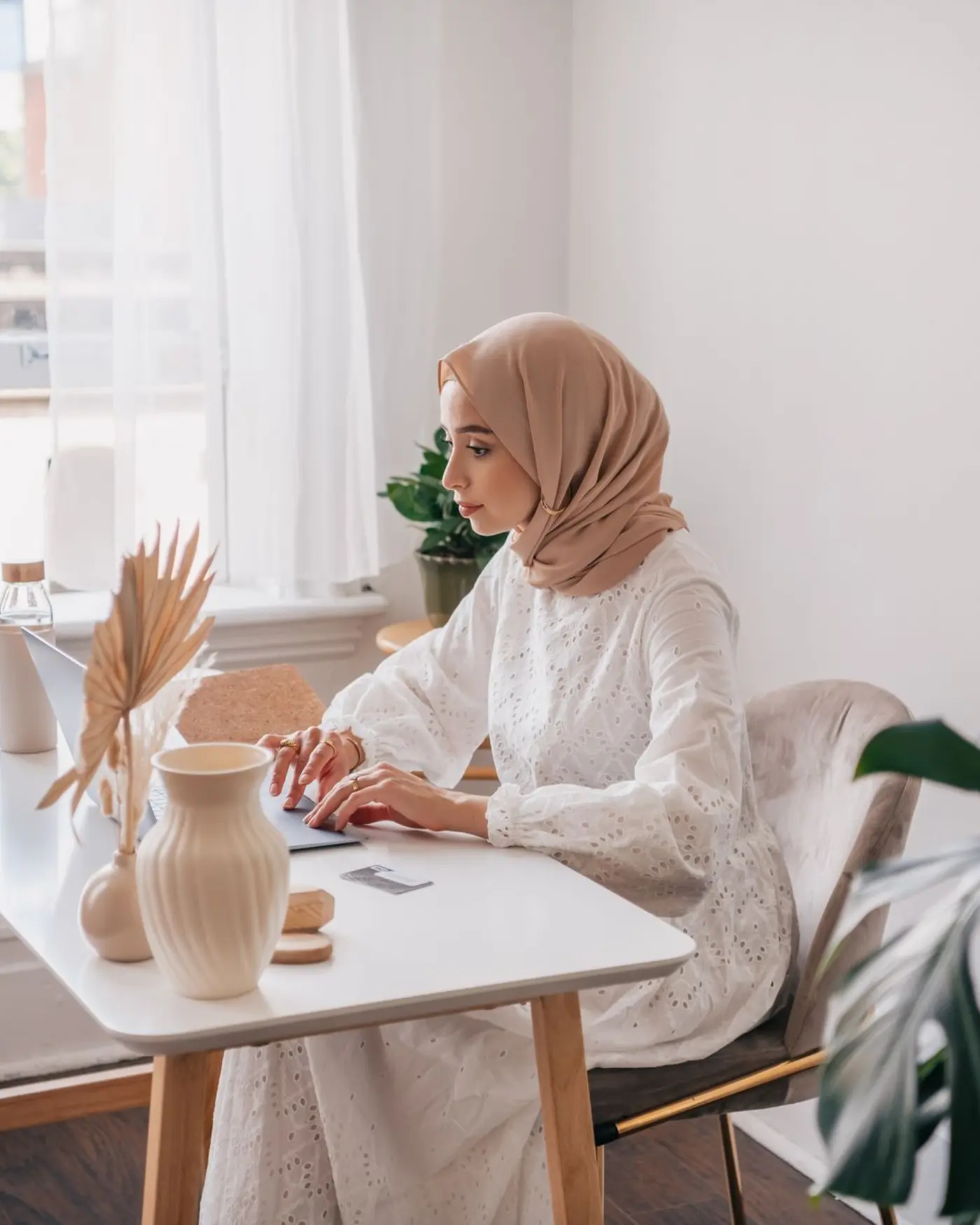 Jonge vrouw met hijab werkt glimlachend vanuit een gezellige thuiswerkplek met laptop